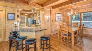 A wooden cabin interior with a kitchen, dining area, and bar stools. - 5 Sleeping Area Log Cabin in a Great Location (Blowing Rock)