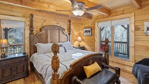 A wooden cabin bedroom with a large bed, a ceiling fan, and a view of the outdoors through a window. - 5 Sleeping Area Log Cabin in a Great Location (Blowing Rock)