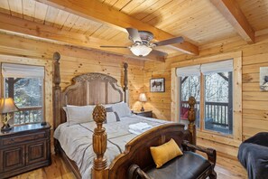 Une chambre dans une cabane en bois, avec un grand lit, un ventilateur de plafond et une vue sur l’extérieur par une fenêtre.
