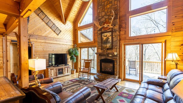 A log cabin interior with a stone fireplace, leather furniture, and large windows. - 5 Sleeping Area Log Cabin in a Great Location (Blowing Rock)