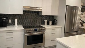 Eine moderne Küche mit weißen Schränken, einem Edelstahlherd, einem eingebauten Backofen und einem Kühlschrank.