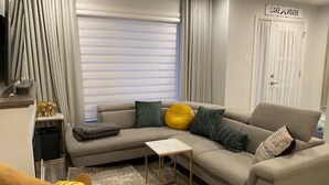 Ein modernes Wohnzimmer mit einem beigefarbenen Sofa, einem kleinen weißen Beistelltisch und einem gelben Sessel.