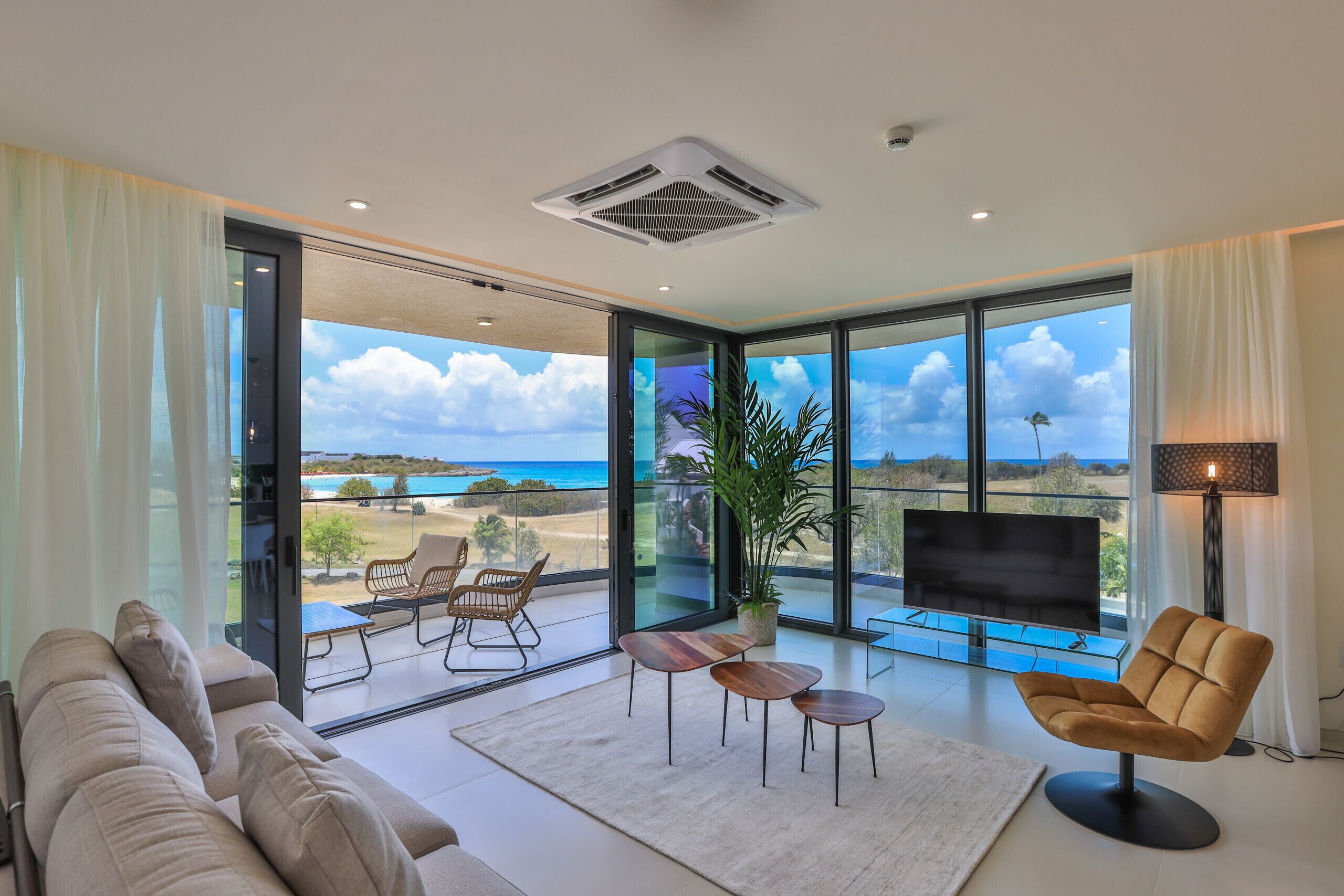 Een moderne woonkamer met een grote televisie, comfortabele zithoek en uitzicht op het strand.