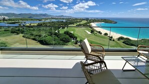 A balcony with wicker chairs and a table, overlooking a beach and golf course with mountains in the background. - A-1303 Wonderful 2  bedroom apartment right in front of Mullet Bay Beach (Cupecoy)