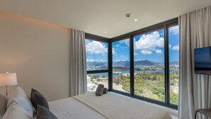 A bedroom with a large bed, a TV, and a view of a lake and mountains. - A-1303 Wonderful 2  bedroom apartment right in front of Mullet Bay Beach (Cupecoy)