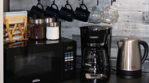 Eine Küche mit Mikrowelle, Kaffeemaschine, Wasserkocher und verschiedenen Küchengeräten an einer Holzwand.