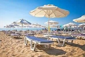 Uma praia com fileiras de espreguiçadeiras e guarda-sóis.