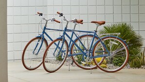 A modern outdoor area with a white tiled wall, two bicycles, and a palm tree. - Twin Palms Resort - A Gay Men's Resort (Palm Springs)