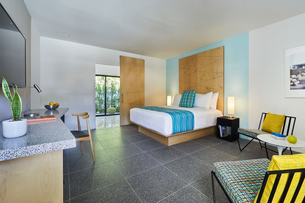 Een moderne hotelkamer met een groot bed, een bureau, een stoel, een bijzettafeltje en een plant in pot.