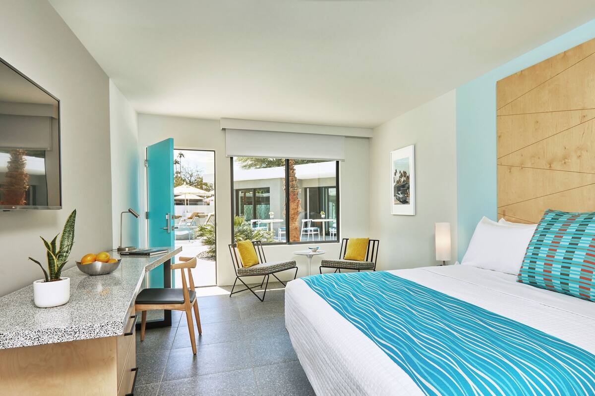 Een moderne hotelkamer met een bed, een bureau en uitzicht op het buitenzwembad.