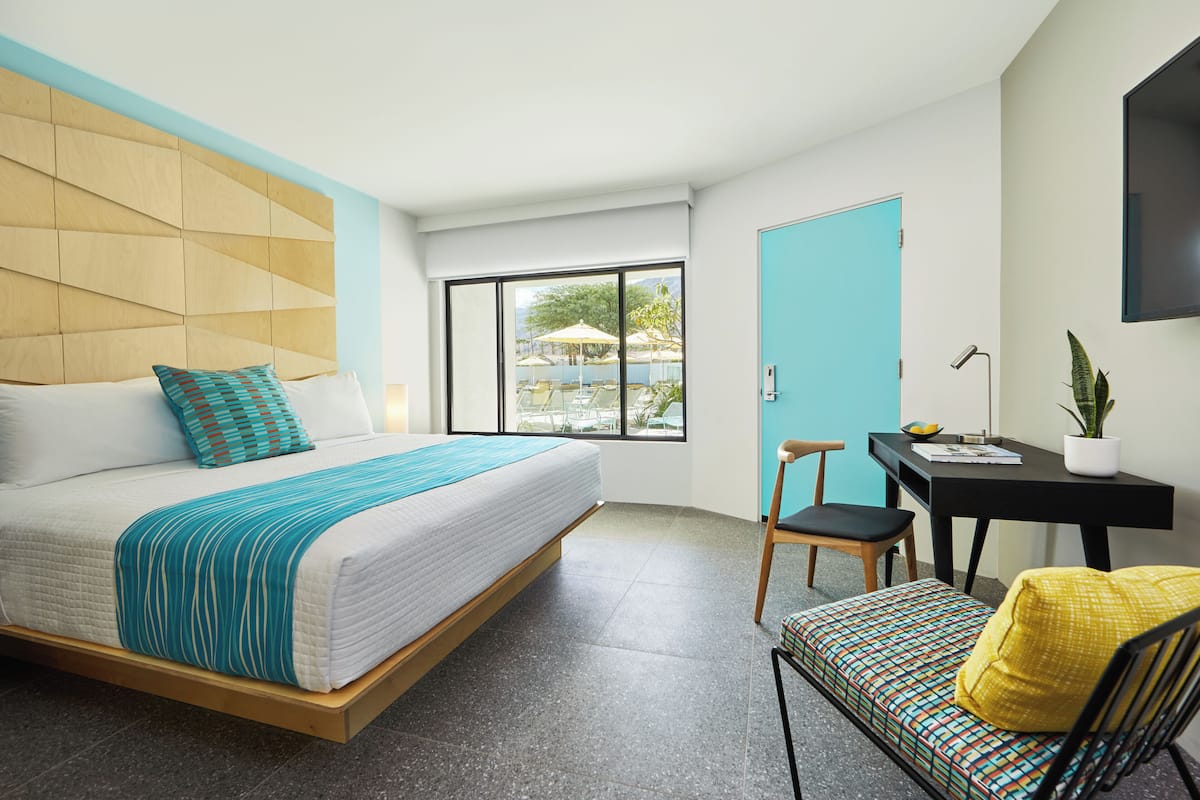 Een moderne hotelkamer met een bed, een bureau, een stoel en uitzicht op het buitenleven.