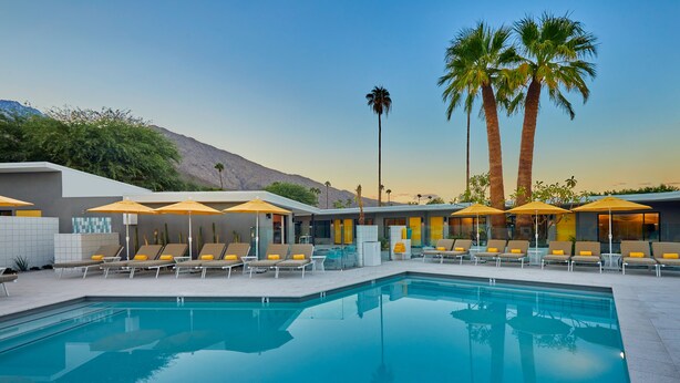 A pool area with lounge chairs and umbrellas, a mountain backdrop, and a clear sky. - Twin Palms Resort - A Gay Men's Resort (Palm Springs)