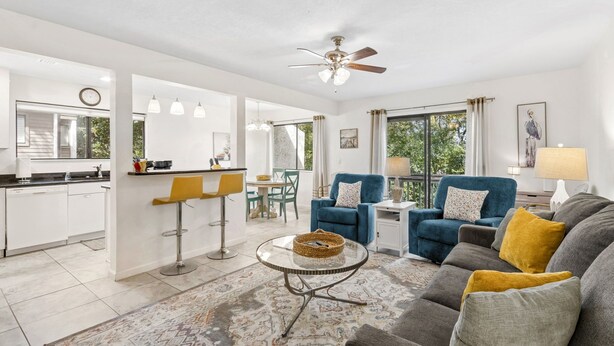 A modern living room with a sofa, two armchairs, a coffee table, and a dining area with a kitchen in the background. - Sea Glass Cove - Hosted By Moore AI Rentals (Fernandina Beach)