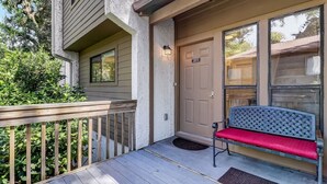 A wooden deck with a bench, a door with a number plate, and a mailbox. - Sea Glass Cove - Hosted By Moore AI Rentals (Fernandina Beach)