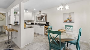 A modern kitchen with white cabinets, a dining area with teal chairs, and a glass-top table. - Sea Glass Cove - Hosted By Moore AI Rentals (Fernandina Beach)
