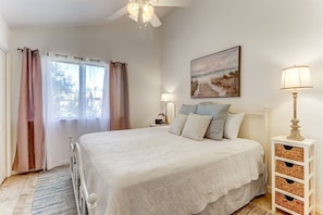A bedroom with a bed, a nightstand, a lamp, a picture on the wall, and a window with curtains. - Sea Glass Cove - Hosted By Moore AI Rentals (Fernandina Beach)