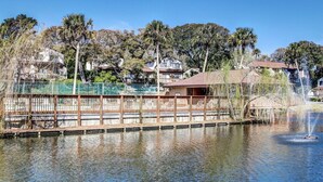 A waterfront area with a wooden dock, a fountain, and residential buildings in the background. - Sea Glass Cove - Hosted By Moore AI Rentals (Fernandina Beach)