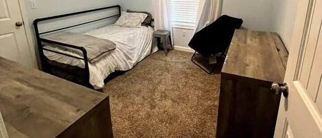 Un dormitorio con una cama individual, ventilador de techo, ventana con cortinas y cómoda.