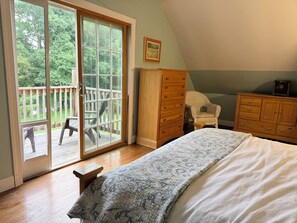 Un dormitorio con una cama grande, un aparador de madera, una silla y un amplio ventanal corredizo que da a una terraza.