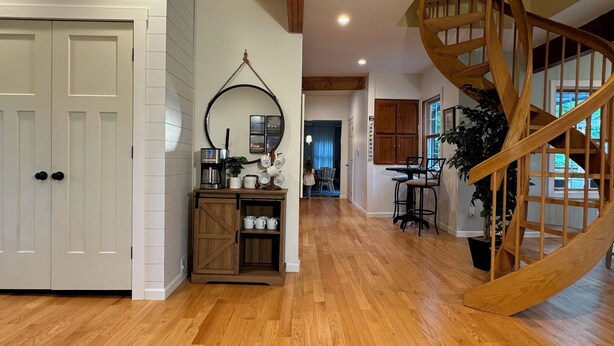 A spacious hallway with wooden flooring, a white door, a coffee station, and a spiral staircase. - Family Lake Getaway on Davis Stream  5BR + Kayaks (Jefferson)
