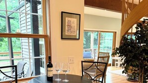 A dining area with a round table, four chairs, a bottle of wine, and two glasses. There is a framed picture on the wall and a staircase in the background. - Family Lake Getaway on Davis Stream  5BR + Kayaks (Jefferson)
