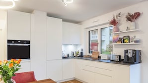 Una cocina moderna con armarios blancos, horno empotrado, cafetera y ventana con vistas a un balcón.