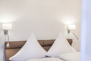 A hotel room with a brown headboard, two white pillows, and wall-mounted lamps.