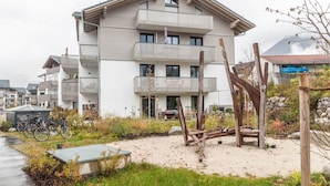 Un edificio de varios pisos con balcones, un área de suelo arenoso y bicicletas.