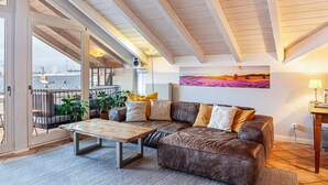 Een gezellige woonkamer met een grote bruine leren bank, een houten bijzettafeltje en een uitzicht door een glazen deur op een buitenbalkon.