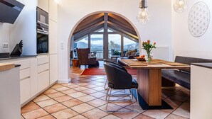 Een moderne keuken met een centraal eiland, een eethoek met een bank en een uitzicht door een rondbogig raam.