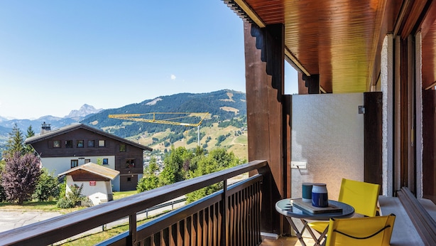 A balcony with a view of mountains, a table with chairs, and a building in the background. - Au Soleil De Megève 750m From Ski, Megeve (Chamonix), France (Megeve (Chamonix))