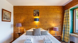 A neatly made bed with two folded towels, a wooden wall with a picture, and two bedside lamps. - Au Soleil De Megève 750m From Ski, Megeve (Chamonix), France (Megeve (Chamonix))
