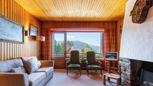 A cozy room with a wooden ceiling, a fireplace, a sofa, two chairs, and a large window with a mountain view. - Au Soleil De Megève 750m From Ski, Megeve (Chamonix), France (Megeve (Chamonix))