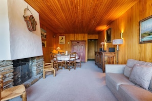 Una sala de estar acogedora con chimenea de piedra, techo de madera y un comedor con mesa y sillas.