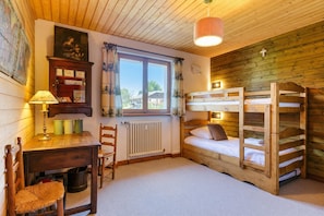 Una habitación de madera con literas, un escritorio, una silla, un radiador y una ventana con cortinas.