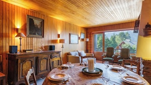 A wooden-paneled room with a dining table set for four, a fireplace, and a large window with a view of a mountain. - Au Soleil De Megève 750m From Ski, Megeve (Chamonix), France (Megeve (Chamonix))
