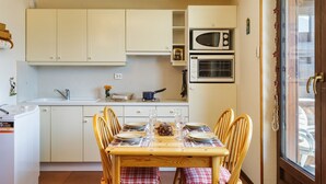 Cocina compacta con armarios blancos, microondas y una mesa de comedor preparada para cuatro personas.