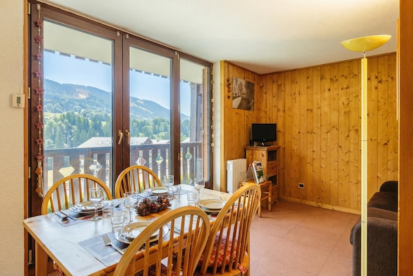 A dining area with a table set for four, a television, and a view of the outdoors. - View Sur Arly E10, Megeve (Chamonix), France (Megeve (Chamonix))