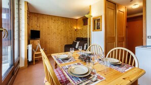 Un comedor con una mesa de madera dispuesta para cuatro, un televisor al fondo y un rincón de estar acogedor con un sofá y sillones.