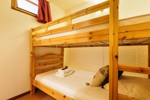 A bunk bed with a lower bunk and a top bunk. There is a window with a curtain, a towel on the lower bunk, and a pillow on the top bunk.