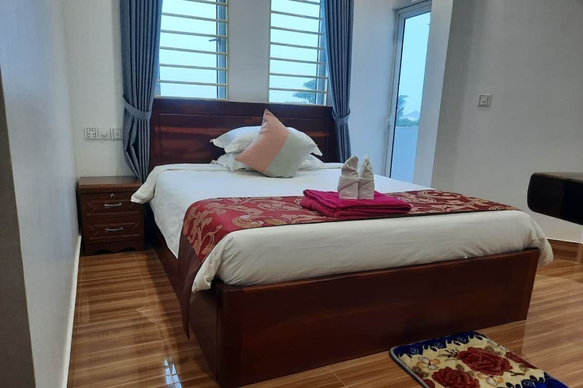 A hotel room with a wooden bed, a bedside table, a nightstand, and a window with curtains.