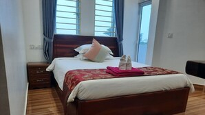 A neatly made bed with a floral bedspread, a wooden nightstand with drawers, and a blue patterned rug on a wooden floor. - Realkhom Villa (Siem Reap)