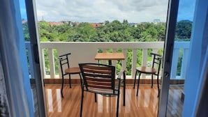 A balcony with a wooden table and chairs, offering a view of greenery and buildings. - Realkhom Villa (Siem Reap)