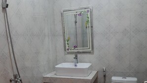 A small bathroom with a white sink, a mirror, a toilet, and a shower. - Realkhom Villa (Siem Reap)