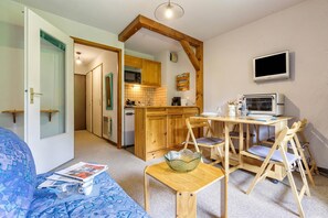 Ein gemütliches Zimmer mit einem Bett, einem kleinen Holztisch, einem Fernseher und einer Küchenzeile.