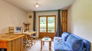 Un espacio habitable compacto con kitchenette, una mesa de comedor, un sofá y una ventana con vista a follaje.