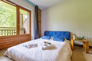 A bedroom with a large bed, a wooden headboard, a small bedside table, and a view of a balcony.