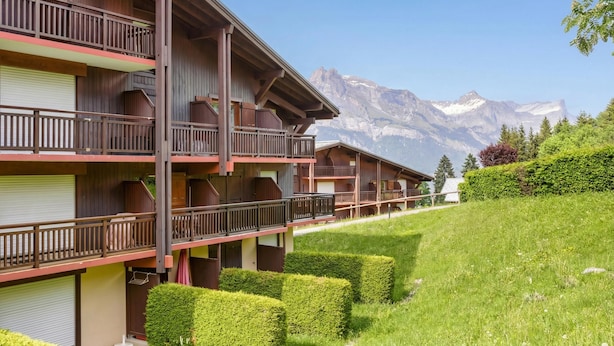 Un hotel de varios pisos con balcones, vistas a la montaña y setos bien cuidados.