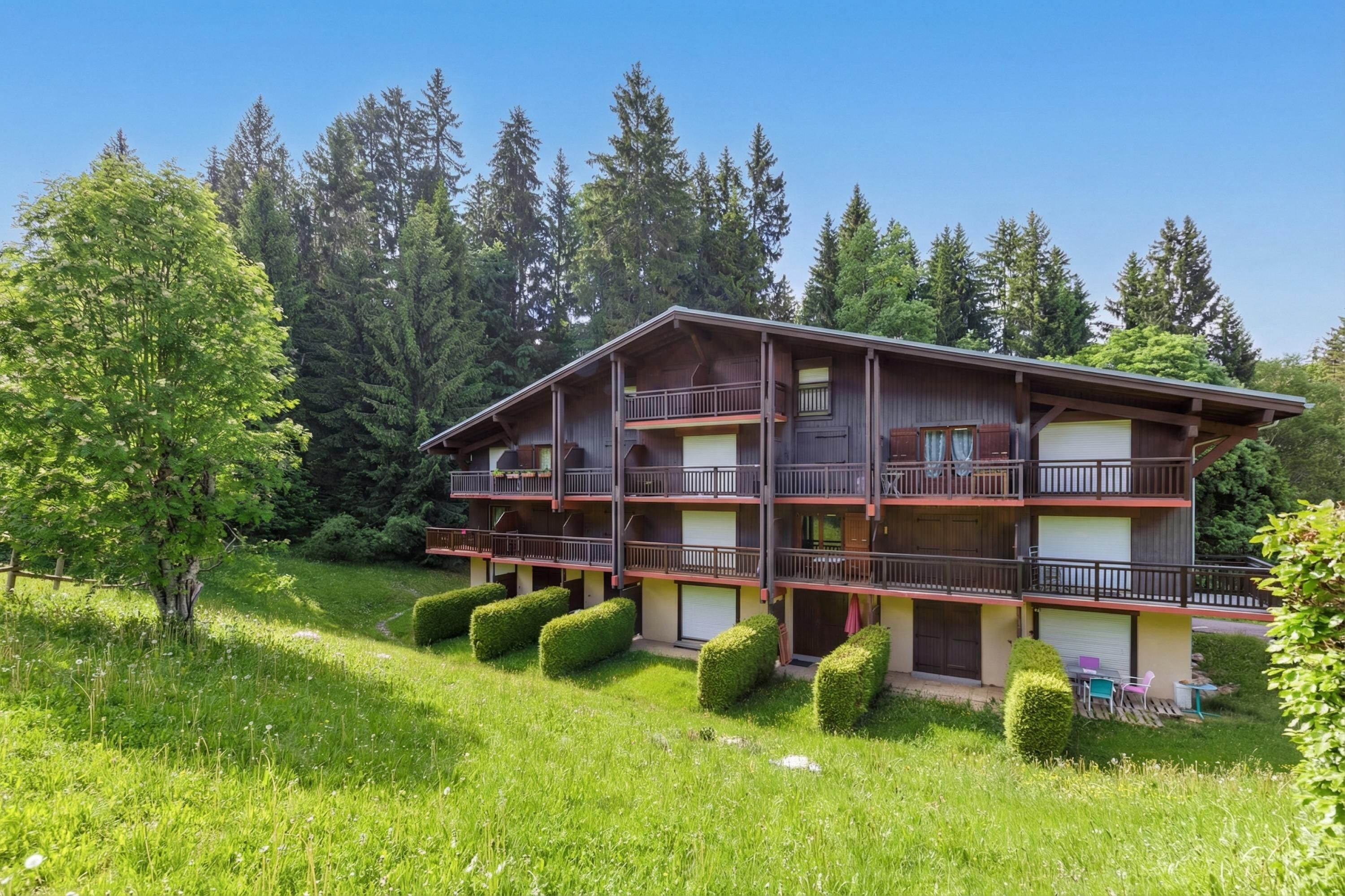 A multi-story chalet with balconies, surrounded by lush greenery and tall trees.