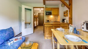 Una habitación acogedora con una mesa de comedor de madera dispuesta para dos, un sofá con una revista y una kitchenette con armarios de madera y un microondas.